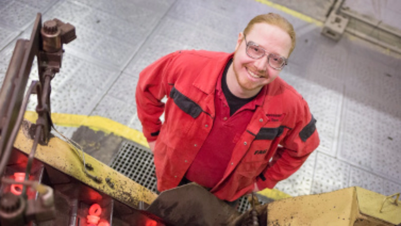 Ein junger Mann in roter Arbeitskleidung blickt lächelnd in die Kamera.