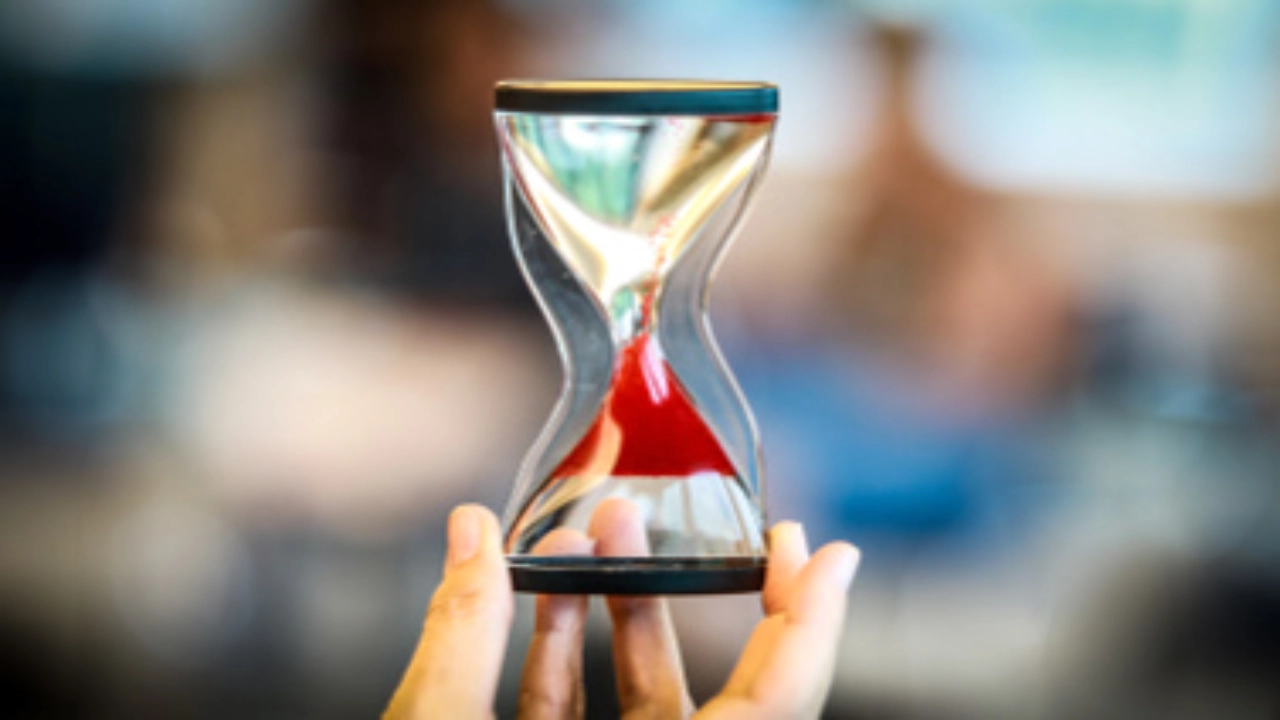 Eins Sanduhr, durch die roter Sand rinnt.