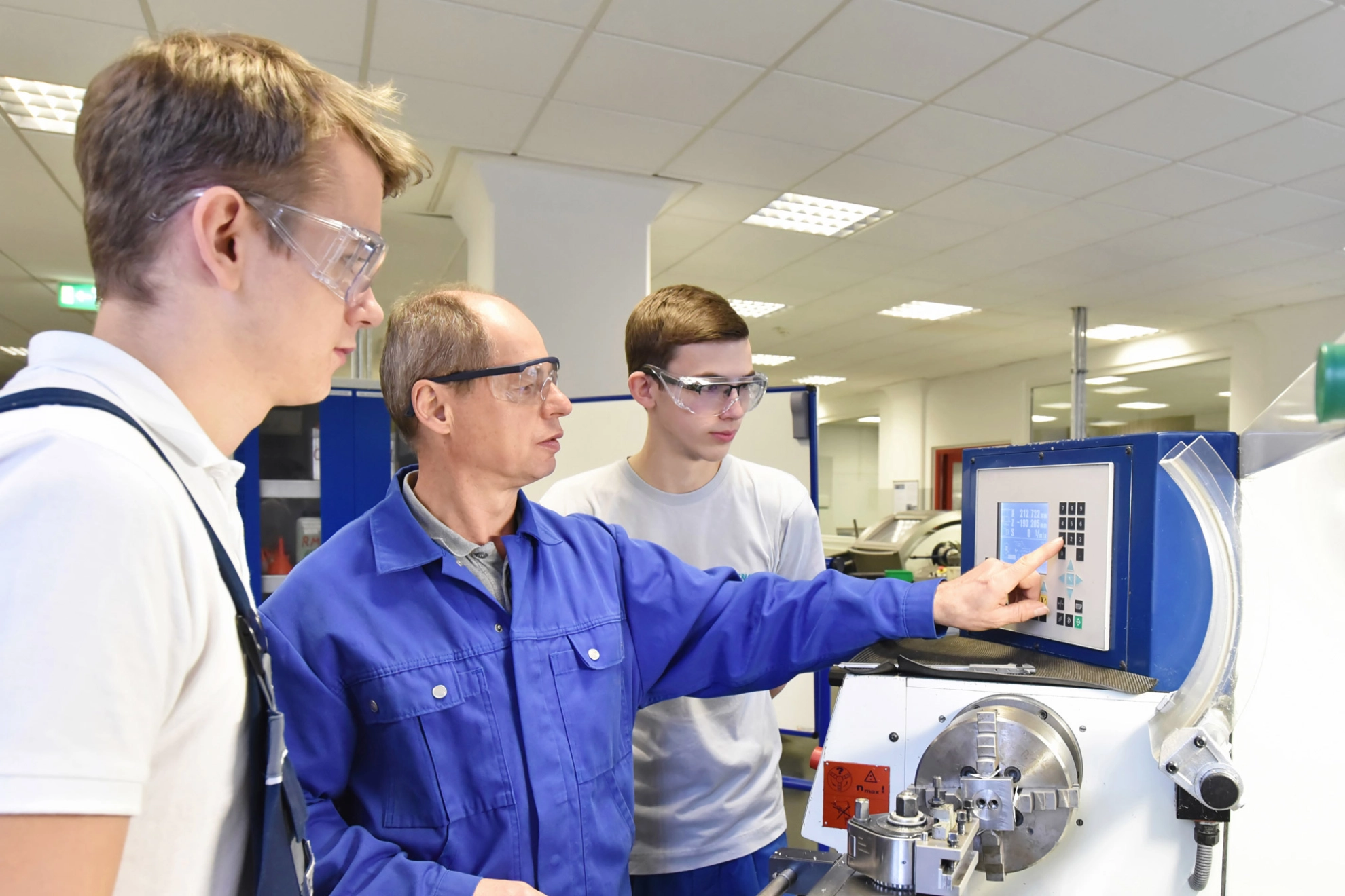 Junge Auszubildende in der technischen Berufsausbildung werden von älteren Trainer auf CNC-Drehmaschinen Maschinen unterrichtet